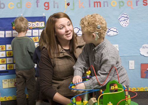 A teacher speaking with a boy who is wearing a cochlear implant in a preschool setting